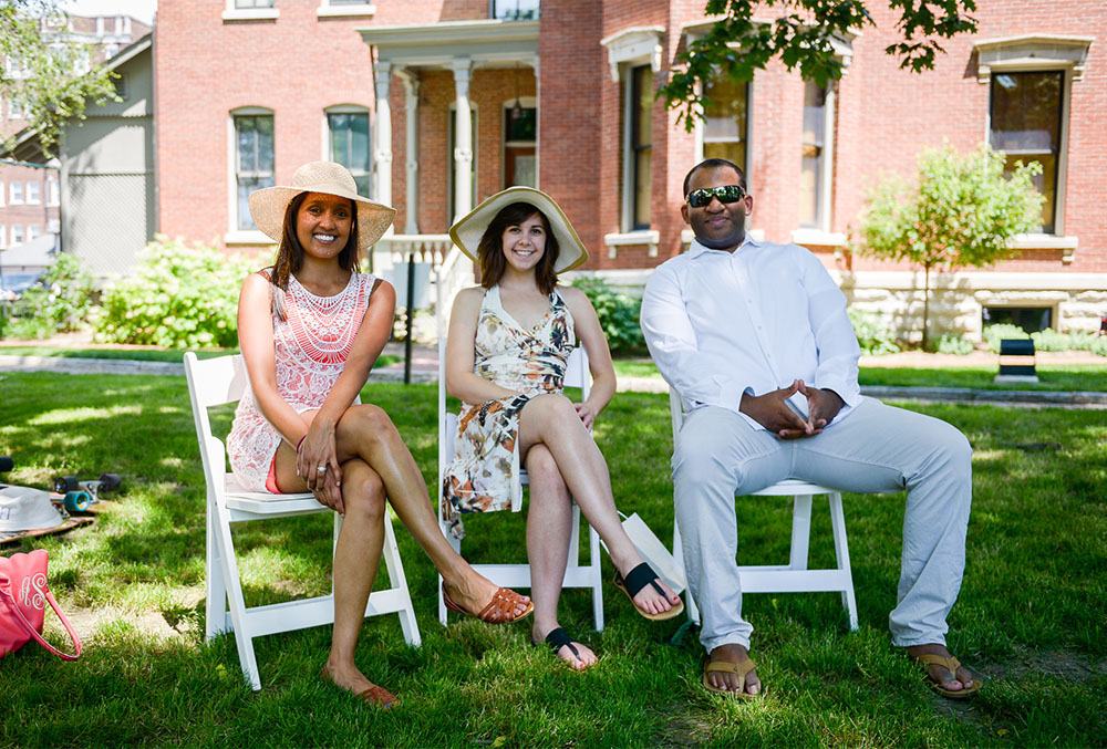 Photograph of two females and one male relaxing on the front lawn of the presidential site, in white chairs. Each subject sporting a broad smile.