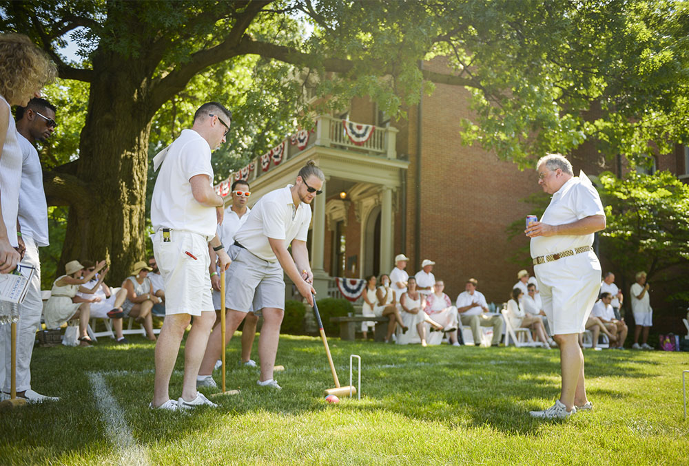 Photograph of people playing croquet on the lawn of the Presidential Site, all dressed in white on a warm sunny day.