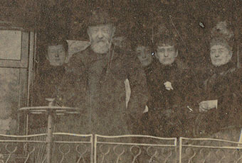 Damaged early photograph of the Harrison family, gathered on a train. Benjamin Harrison stands before the family, sporting his signature top hat and facial hair.
