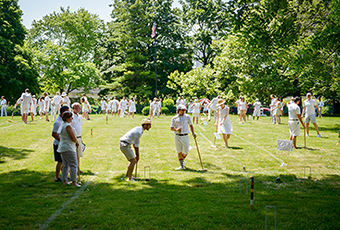 Image of 30 people dressed in white playing croquet on a green lawn