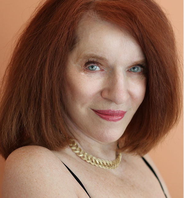 Portrait of Donna Wing. An older woman with red hair, green eyes, red lipstick, and a gold necklace.