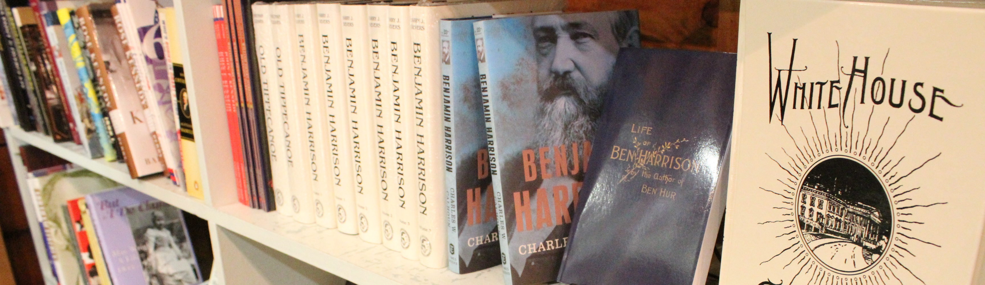 A bookshelf lined with many of the books sold at the presidential site gift shop. Featured in the image is the White House Cookbook the life of Benjamin Harrison, and several other books about the president.