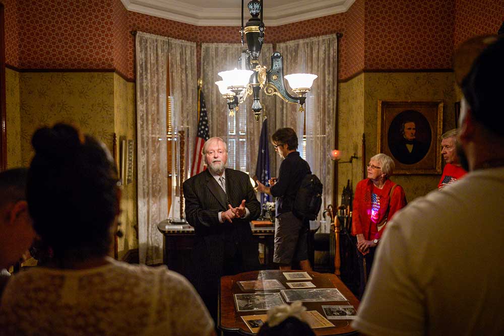 photograph of an actor playing benjamin harrison, conferring with a tour group in his office space.