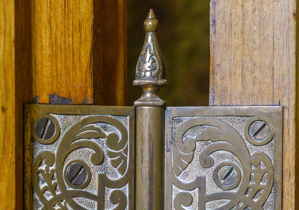 Ornate Victorian door hinge at the Benjamin Harrison Presidential Site. The patterning shows several curves bursting outward from a single origin point. The door hinge shows some signs of age.